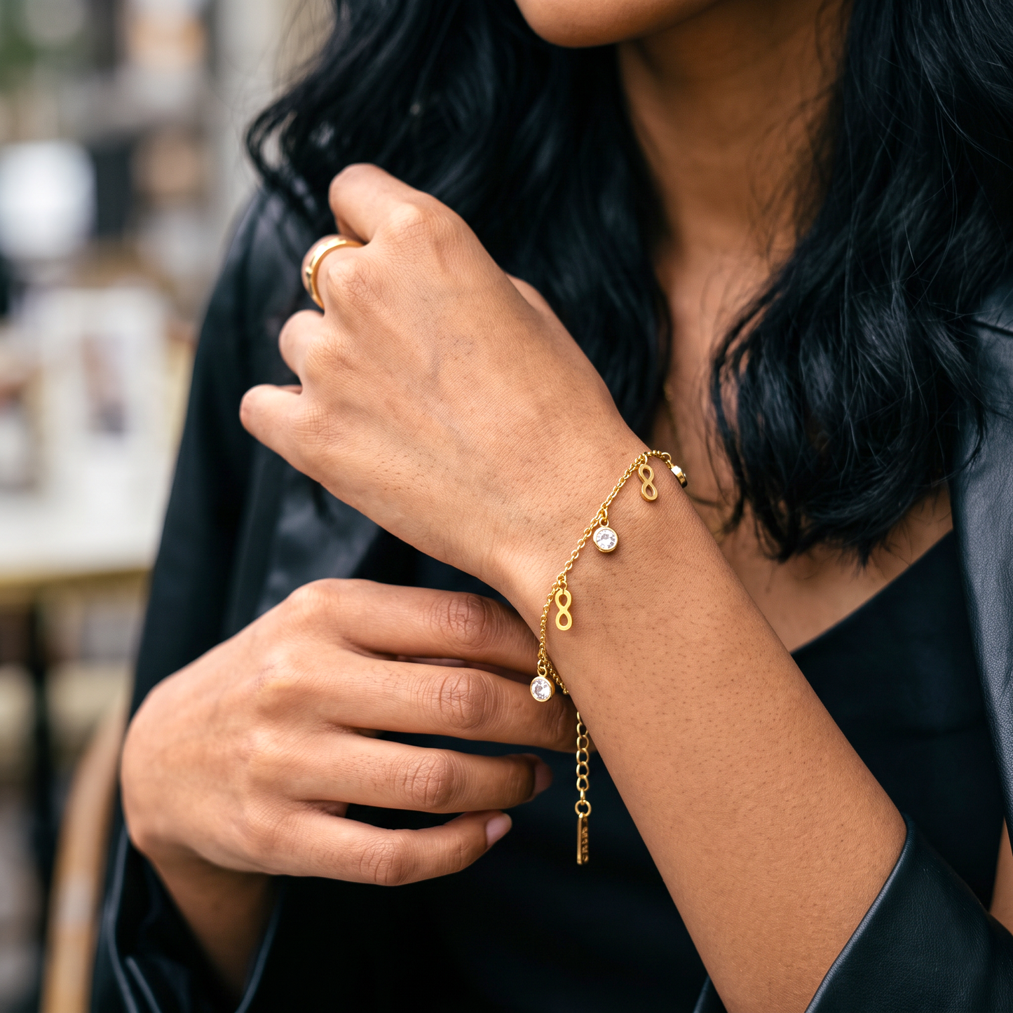 AVIRI gold-tone infinity charm bracelet with clear cubic zirconia stones worn on a woman's wrist