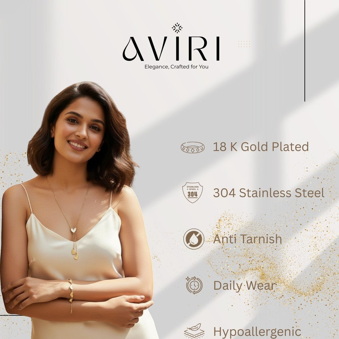 AVIRI gold-tone stainless steel necklace and bracelet set with heart charms. Necklace has lariat design with central heart pendant. Bracelet has small heart accents. Model wears set with a cream slip dress.