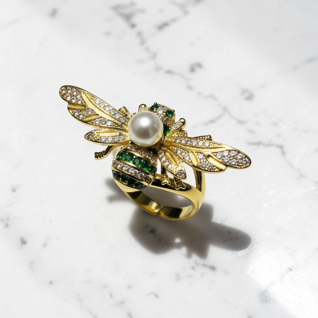 AVIRI gold-tone bee ring with pearl body, emerald accents, and cubic zirconia wings. Adjustable.