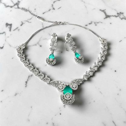 AVIRI emerald green gemstone and clear stone statement necklace and earring set with intricate detailing.