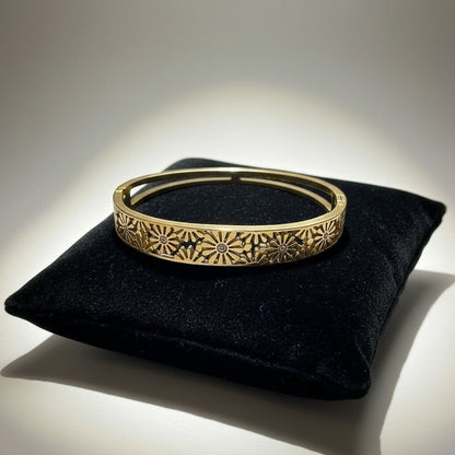 AVIRI gold-tone hinged bangle bracelet with intricate floral cut-out detailing and a polished finish.
