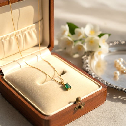AVIRI gold-plated necklace with a rectangular emerald-cut green stone pendant on a delicate chain, presented in a wooden jewelry box.