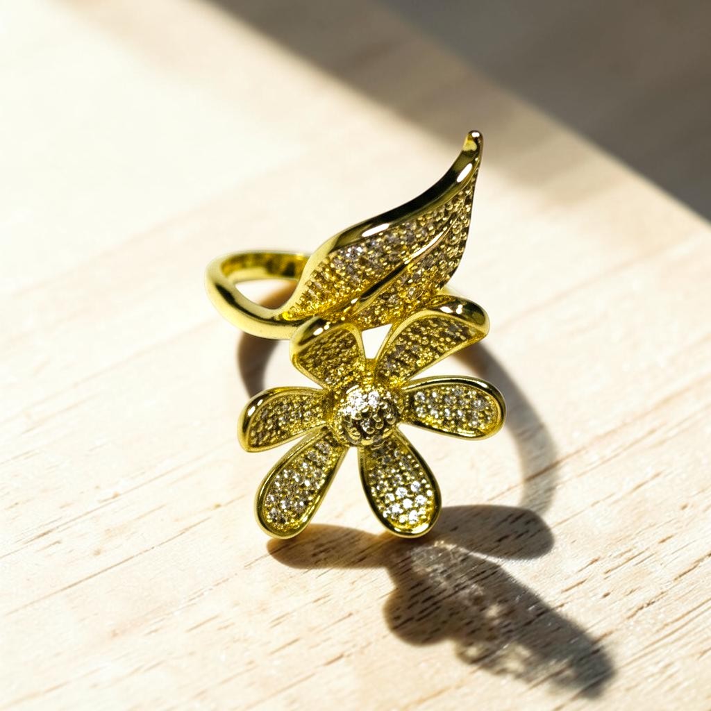 AVIRI gold-tone adjustable ring with a daisy flower and leaf motif, encrusted with cubic zirconia stones.