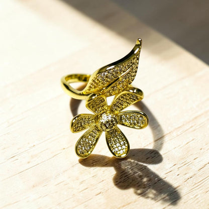 AVIRI gold-tone adjustable ring with a daisy flower and leaf motif, encrusted with cubic zirconia stones.