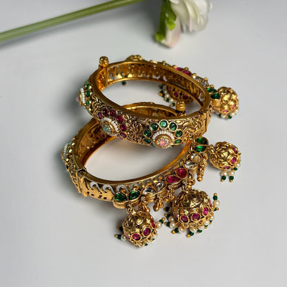 AVIRI traditional gold-tone hinged bangle bracelets with red and green Kundan stones and dangling jhumka charms.