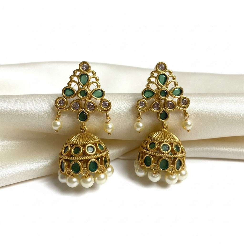 AVIRI gold tone jhumka earrings with emerald green stones and pearl drops. Intricate detailing on bell shape.