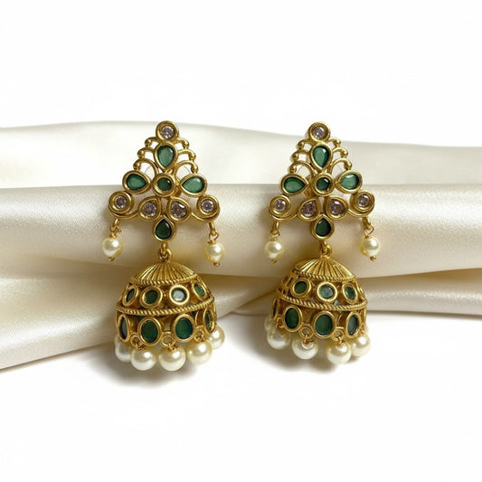 AVIRI gold tone jhumka earrings with emerald green stones and pearl drops. Intricate detailing on bell shape.