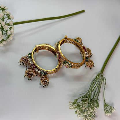 AVIRI traditional gold-tone hinged bangle bracelets with red and green Kundan stones and dangling jhumka charms.