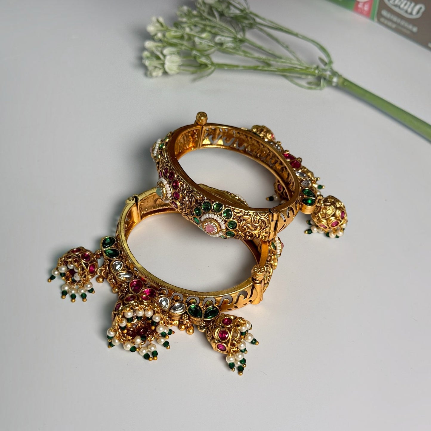 AVIRI traditional gold-tone hinged bangle bracelets with red and green Kundan stones, floral filigree, and dangling jhumkas