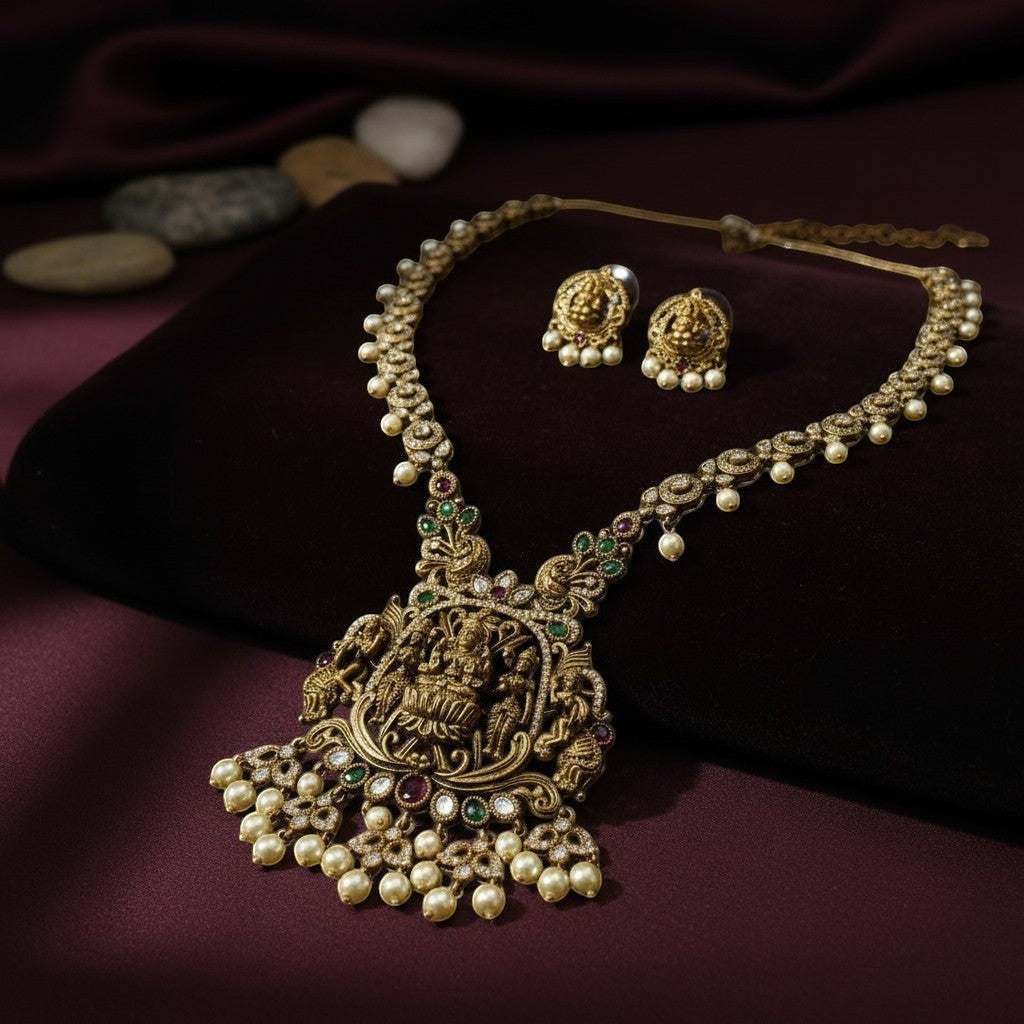 AVIRI gold-plated Lakshmi pendant necklace and earrings set with pearls, green and red stones. Antique finish.