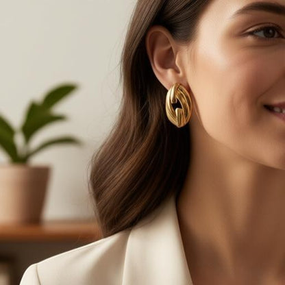 AVIRI oval link statement stud earrings in 18K gold plated stainless steel worn by a woman in a blazer